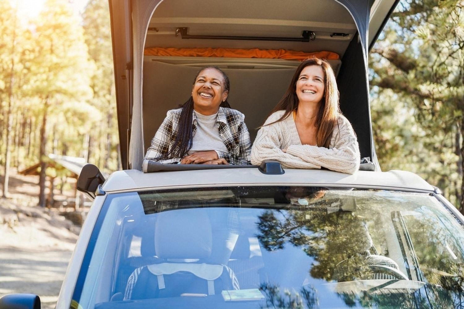 Two women smiling from the rooftop of a rental campervan parked in an Australian forest